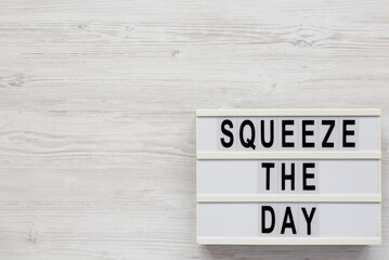 'Squeeze the day' on a lightbox on a white wooden surface, overhead view. Flat lay, top view, from above. Space for text.