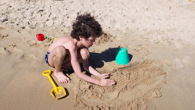 On a Sunny summer day, a child male brunette plays with a toys on a sandy beach