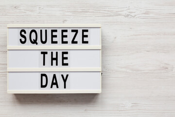 'Squeeze the day' on a lightbox on a white wooden background, overhead view. Flat lay, top view, from above.