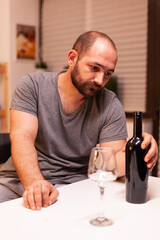 Man holding bottle of red wine being disappointed because of unfaithful wife. Unhappy person disease and anxiety feeling exhausted with dizziness symptoms having alcoholism problems.
