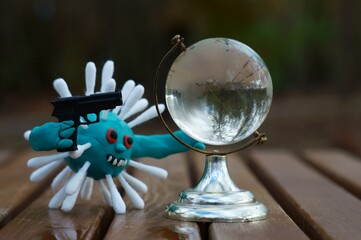 The figure of the virus with a toy gun. Next to it is a small glass globe.