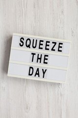 'Squeeze the day' on a lightbox on a white wooden background, overhead view. Flat lay, top view, from above.