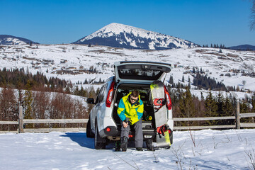 man sitting in car trunk changing for snowboard