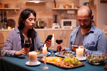 Fototapeta na wymiar Couple dining together using smartphone in kitchen. Adults sitting at the table ,browsing, searching, using smartphones, internet, celebrating anniversary.