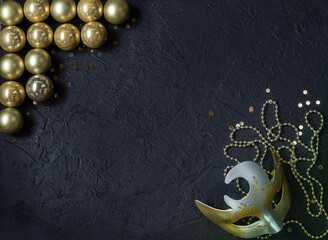 Gold glass balls, carnival mask, sparkles, decorations on a black background. Christmas decor.Place for signature.