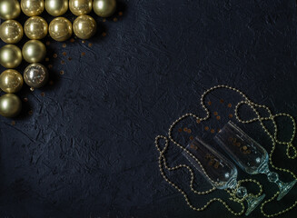 Champagne glasses with sparkles, gold glass balls, decorations on a black background. Christmas decor. Place for signature.