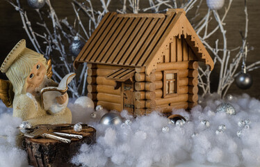 Model of a wooden house with a figurine of an angel, a cut from a tree and house keys in artificial snow on a background of white branches with glass balls. Christmas composition.