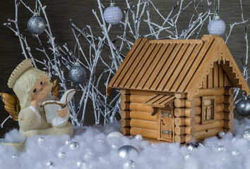 Model of a wooden house with a figurine of an angel in artificial snow on a background of white branches with glass balls. Christmas decor.