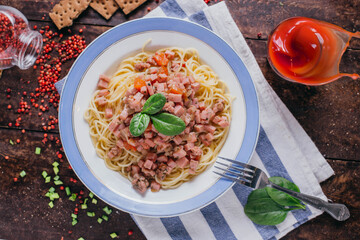 Pasta with ham and tomatoes on the table, restaurant dish on a wooden background