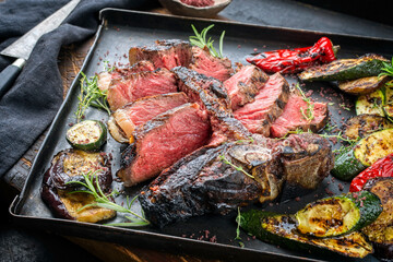 Traditional barbecue dry aged wagyu porterhouse beef steak served with paprika and eggplant as close-up on a rustic metal tray