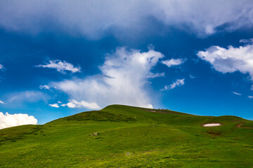 Beautiful mountain landscape at Caucasus mountains with clouds, blue sky and line of horse riders far away