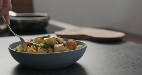 Slow motion add asparagus to pesto fusilli with scallops in blue bowl on concrete countertop