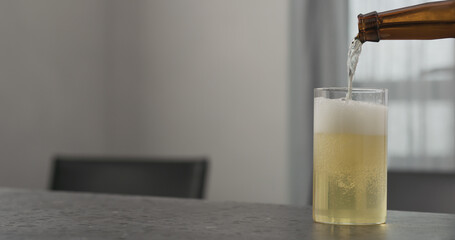 Slow motion pour kombucha into highball glass on concrete countertop with copy space