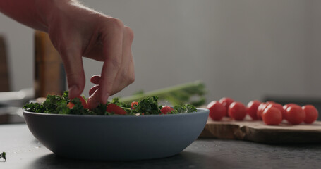 Slow motion man hands put tomatoes on top of kale in blue bowl on concrete surface