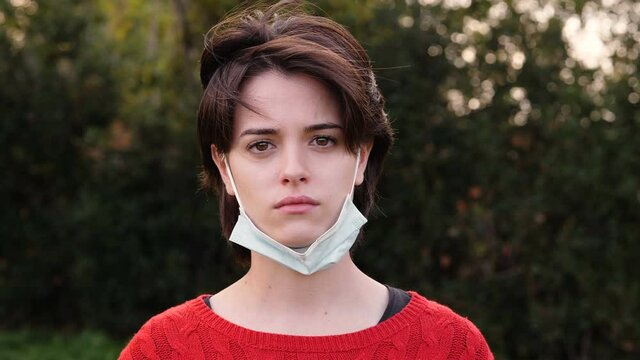 sad worried young woman with the mask pulled down looking serious at camera 