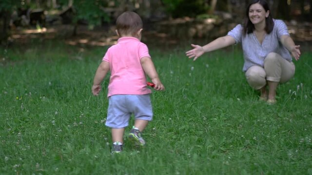 Young mother plays with her son in nature. Baby's first steps. Public park. Camera fly