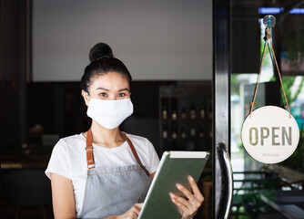 Happy Thai waitress with protective face mask, holding a tablet,  restaurant reopening, Thailand,...