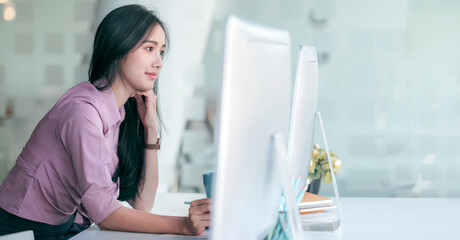 Portrait of young asian woman in casual wear working on personal computer while sitting in modern office, copy space.