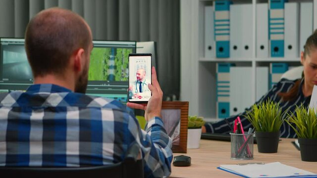 Disabled freelance videographer talking on video call with doctor in work time while creates content sitting in wheelchair in modern company office. Creator blogger working from photo studio.