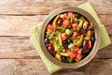 Delicious salad of tomatoes and green peppers Chlada felfel with anchovies and olives close-up in a bowl on the table. horizontal top view from above