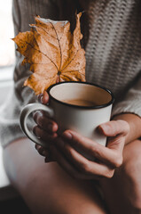 Woman with a cup of coffee and a yellow autumn leaf in her hands