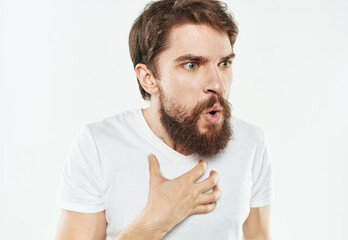 A puzzled man with a beard and in a white T-shirt on a light background