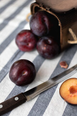 Ripe large plums scattered on a striped tablecloth and chopped plums from a wooden box and a knife