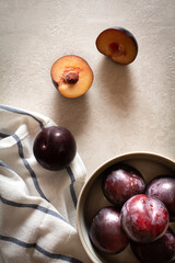 A bowl of ripe plums on a striped napkin and scattered plums on a marble top. Flatlay photo.