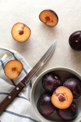 A bowl of ripe plums on a striped napkin and scattered plums and a knife. Flatlay photo.