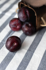 Ripe large plums scattered on a striped tablecloth from a wooden box