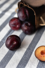 Ripe large plums scattered on a striped tablecloth and chopped plums from a wooden box