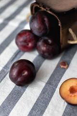 Ripe large plums scattered on a striped tablecloth and chopped plums from a wooden box