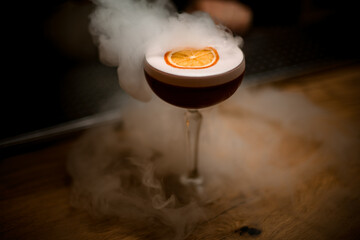 glass of drink with foam and slice of citrus stands on smoky bar counter. © fesenko