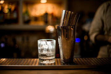 old fashioned glass with ice cubes and shaker stand on the bar