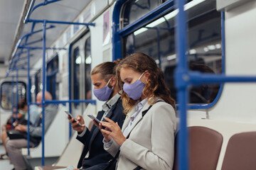 passengers wearing protective masks using their smartphones while sitting in a subway car.