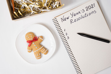 Phrase New Year's Resolutions 2021 in the notebook and pen. Gingerbread man on table