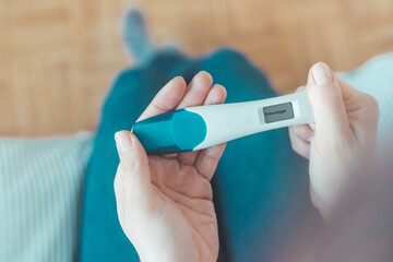 Woman sitting on the bed, checking pregnancy test. Result positive, “Schwanger”