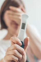 Nervous woman sitting on the bed, checking pregnancy test. Result positive, &ldquo;Pregnant&rdquo;