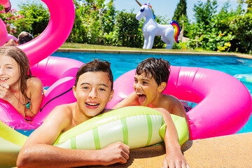 Happy smiling boy in group of children play, have fun in swimming pool outside pose with inflatable doughnut rest enjoying vacation