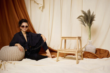 Fashion art photo of beautiful brunette woman in sunglasses, black shirt and trousers in studio interior. soft light