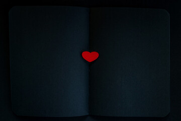 Red heart on an open notebook. Matte black sheets. - 392595614