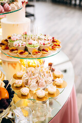 Festive candy bar with cake, macaroons, desserts and fruit decorated with flowers on a round table