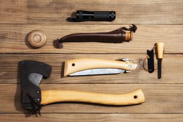 Hiking travel gear on wood backdrop. Flat lay of outdoor travel equipment items. Camping gear including knife, axe, flaslight and saw. 