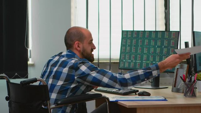 Paralysed manager in wheelchair comparing financial data from documents with colleague working financial corporate building using modern technology. Handicapped disabled businessman analysing graphs