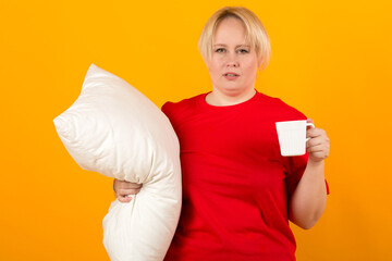 beautiful young plump female in a red t-shirt on a yellow background with a pillow and a mug