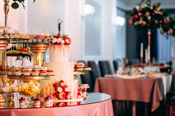 Festive candy bar with cake, macaroons, desserts and fruit decorated with flowers on a round table