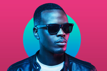 Neon studio portrait of african american man wearing sunglasses and leather jacket isolated on pink background