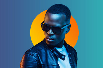 Portrait of stylish black young man wearing leather jacket and sunglasses, isolated on blue...