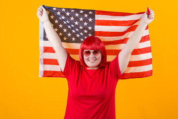 beautiful young plump female with red hair on a yellow background wearing sunglasses with american flag