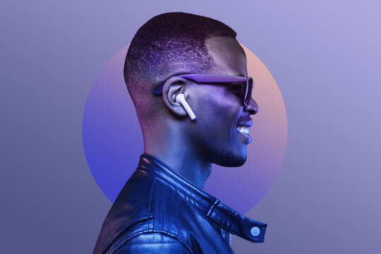 Portrait of smiling african american man listening music with earphones, wearing black leather jacket, isolated on purple background